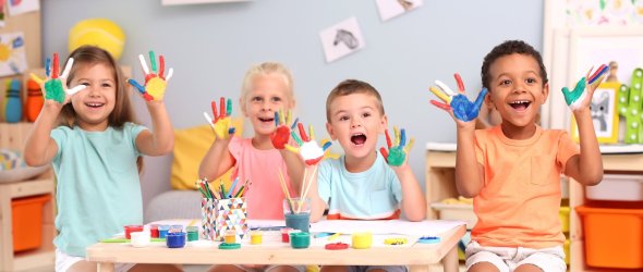 Vier Kinder, die ihre Hände oben haben, mit ganz viel bunter Farbe darauf